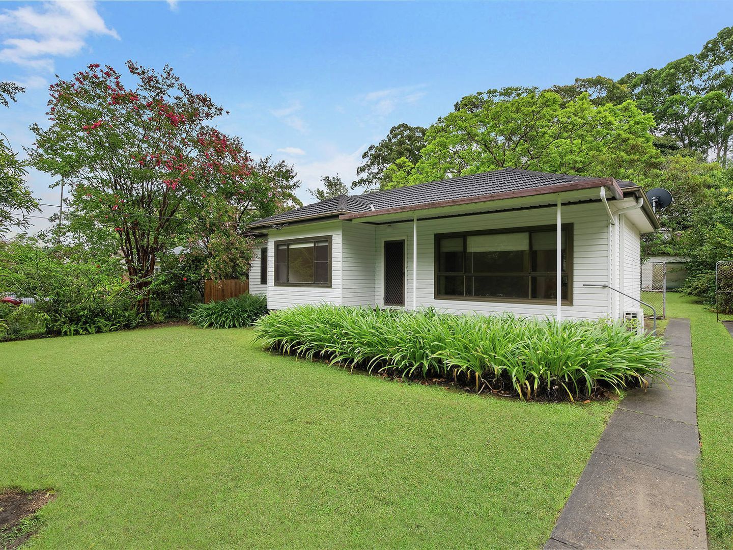 A small white house is sitting on top of a lush green lawn.