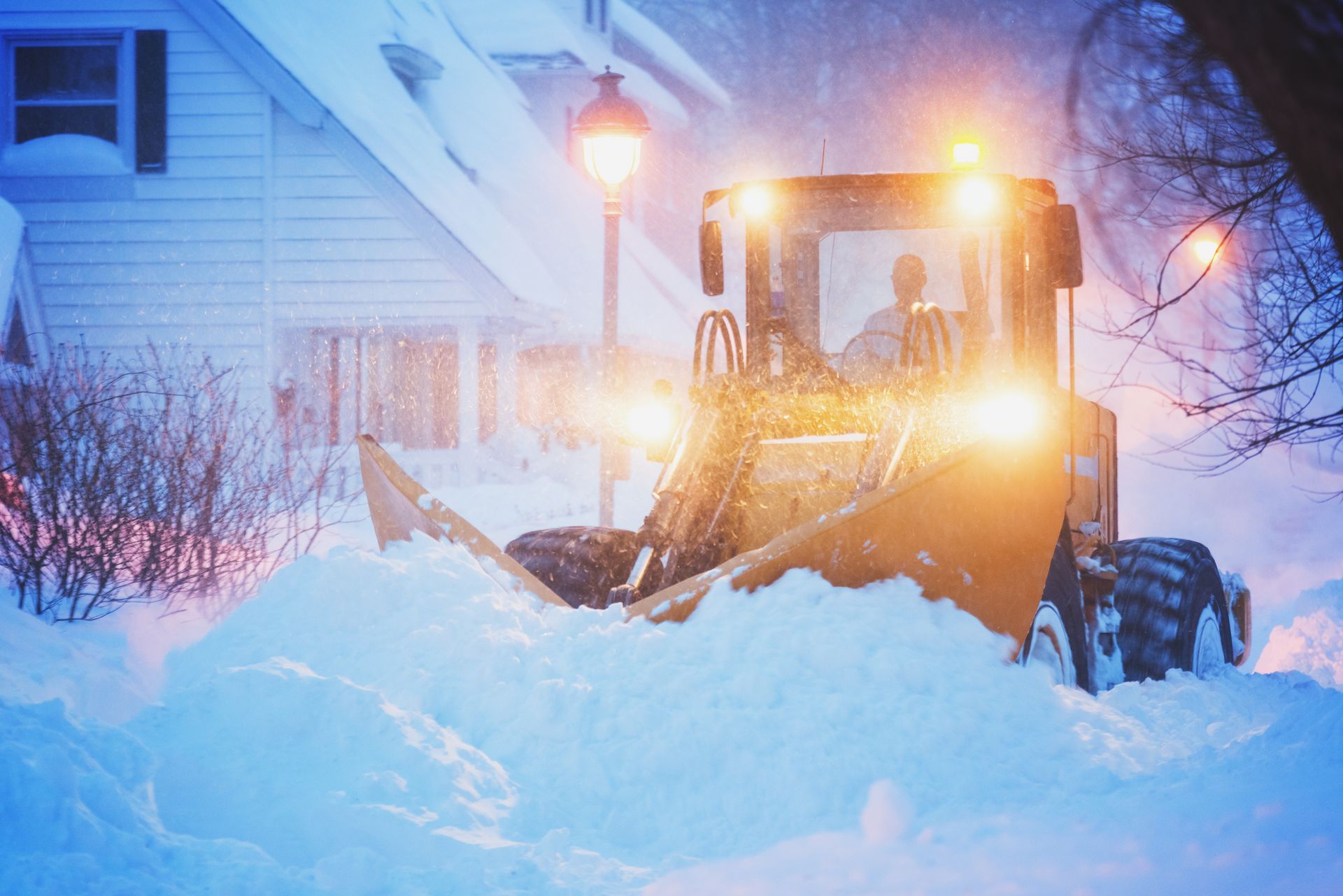 A snow plow is clearing snow in front of a house.