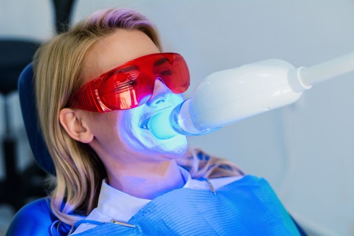 Woman undergoing teeth whitening with blue light in a dental office.