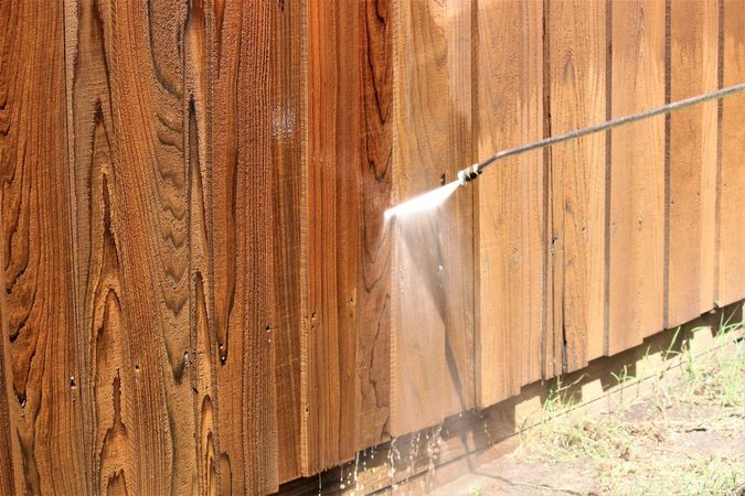 Power washing a weathered wooden fence, showing clean versus dirty areas.