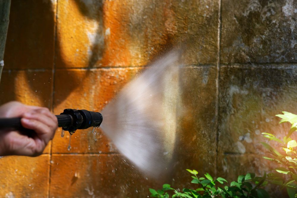 A Person Pressure Washing a Stained Orange Brick Wall — Zac's Bin and Pressure Cleaning In Parramatta Park, QLD