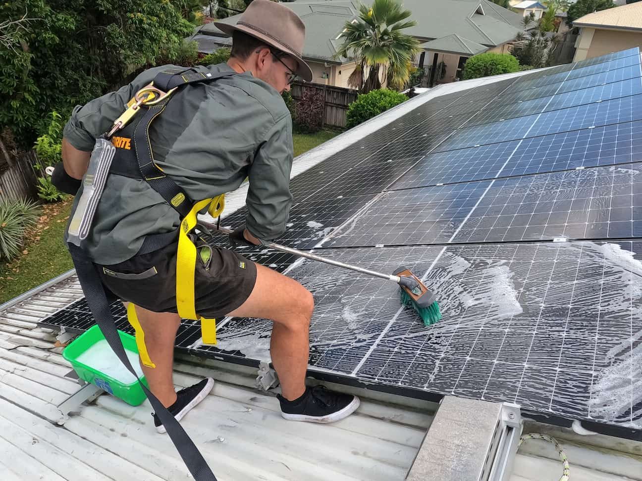 A Man Is Cleaning Solar Panels on The Roof of A House — Zac's Bin and Pressure Cleaning In Parramatta Park, QLD