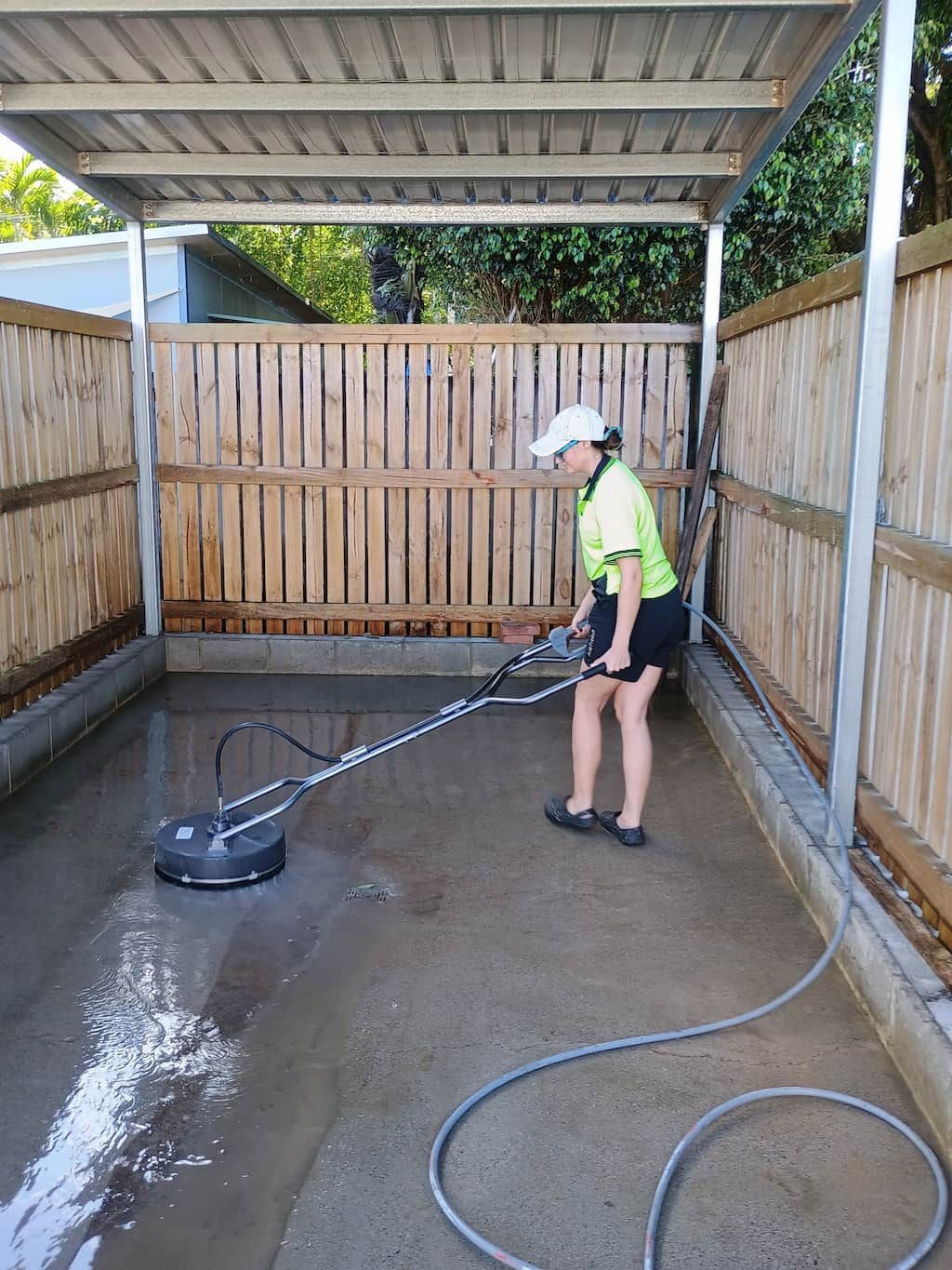 A Woman Is Using a Pressure Washer to Clean a Driveway — Zac's Bin and Pressure Cleaning In Parramatta Park, QLD