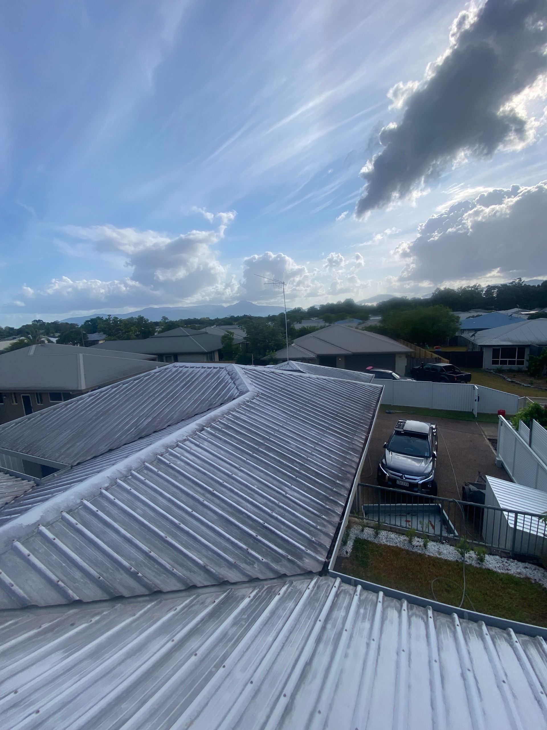 A Person Is Cleaning a Gutter of Leaves from A Roof — Zac's Bin Cleaning & Pressure Washing Services In Parramatta Park, QLD