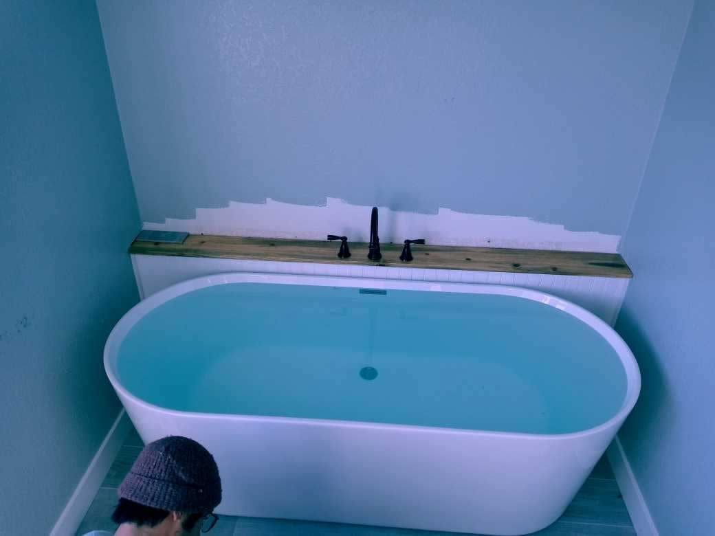 Freestanding bathtub in a partially renovated bathroom with bare wall and exposed trim.