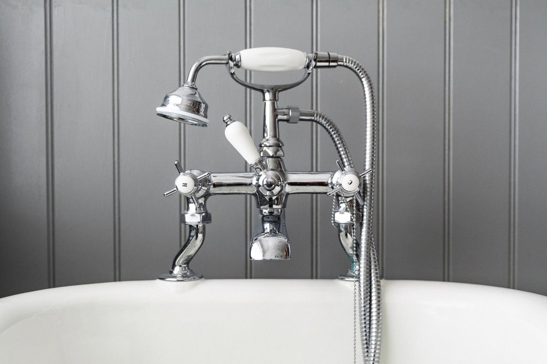 Chrome clawfoot tub faucet with handheld showerhead against a gray tiled wall