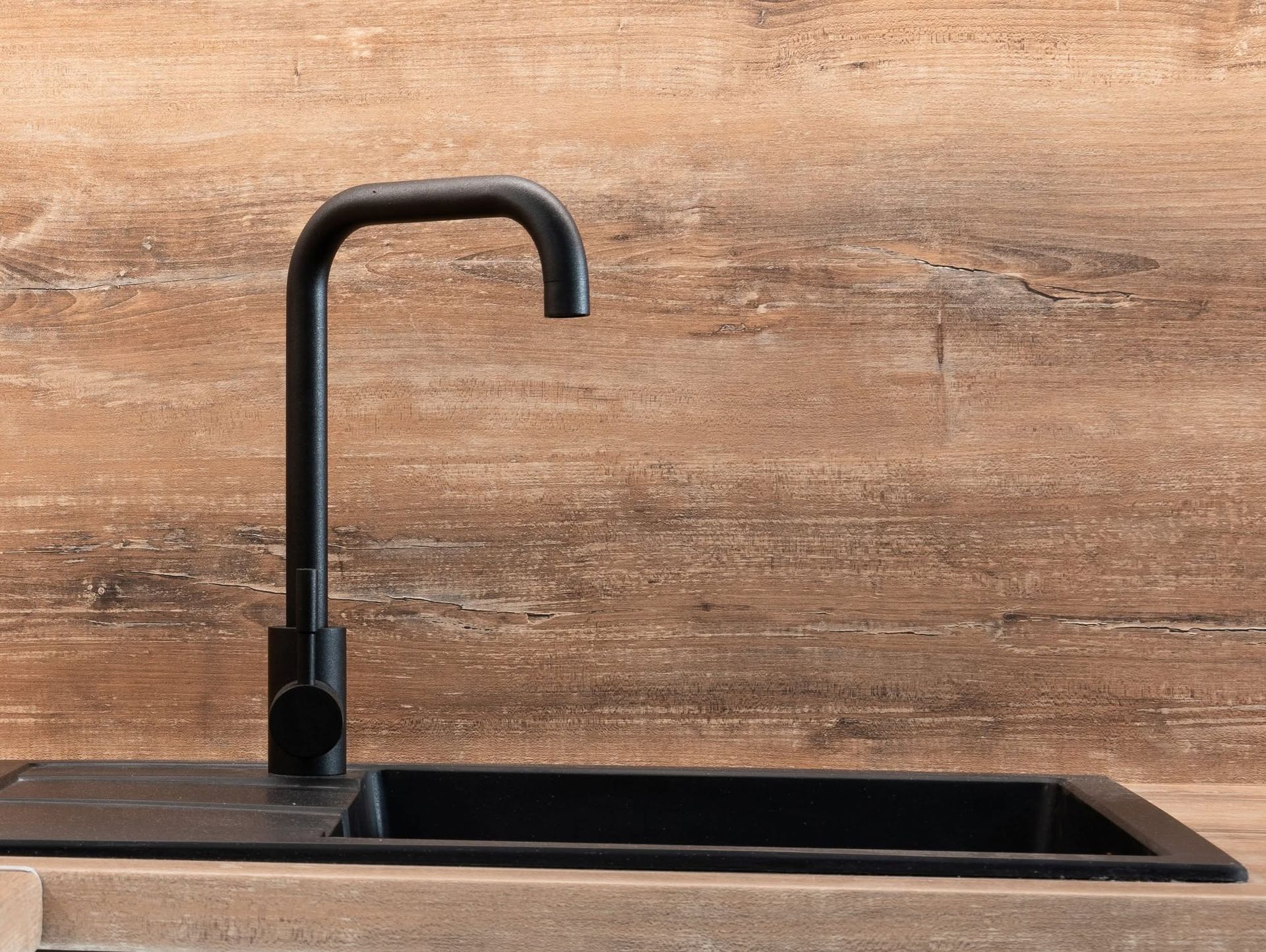 Black kitchen faucet over a black sink on a wooden countertop.