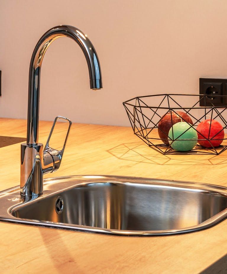 Kitchen sink with chrome faucet and fruit basket on a wooden countertop