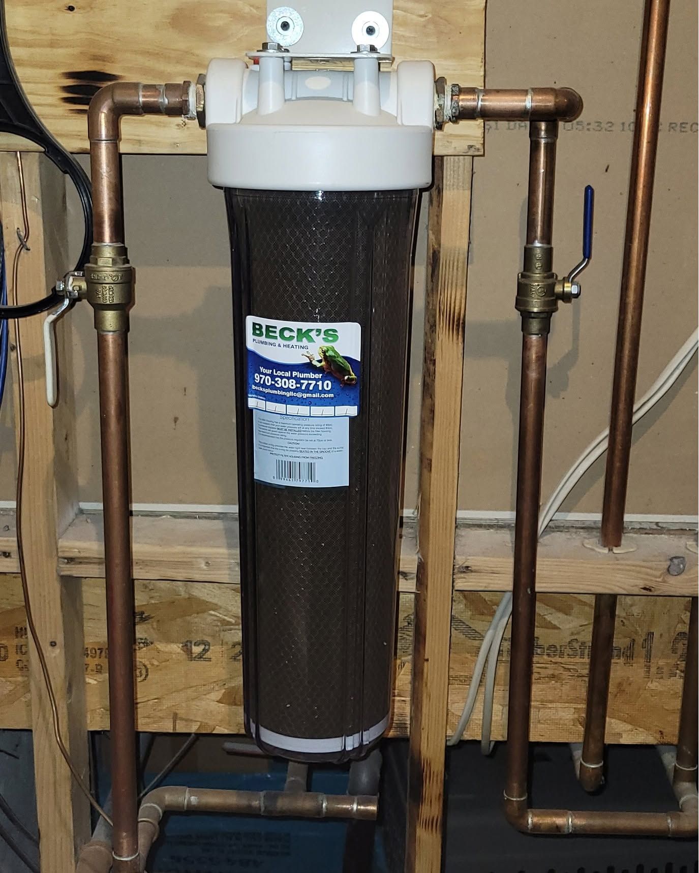 Whole-house water filter canister with black cartridge attached to copper plumbing in a basement.