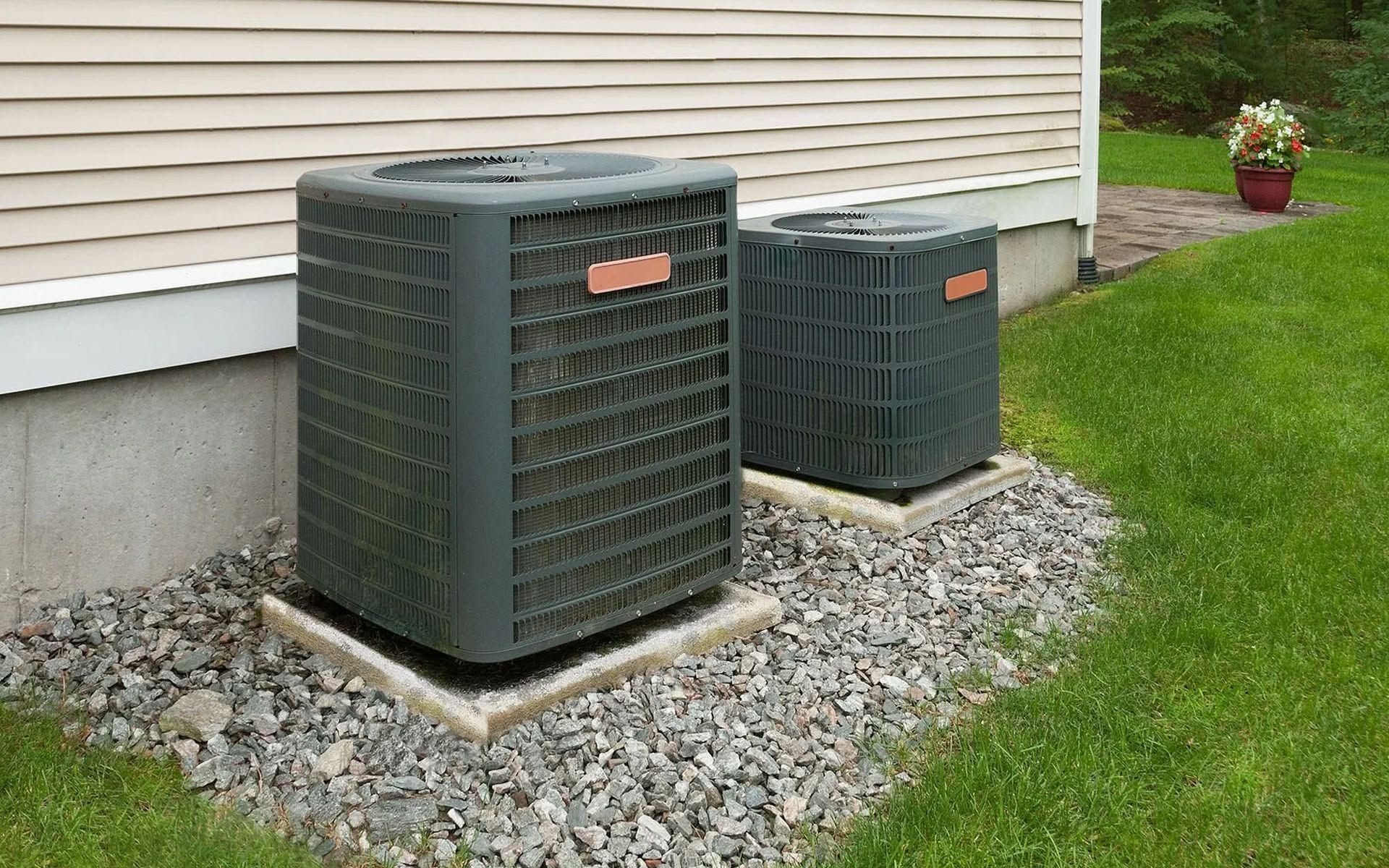 Two outdoor air conditioning units beside a house on a gravel bed