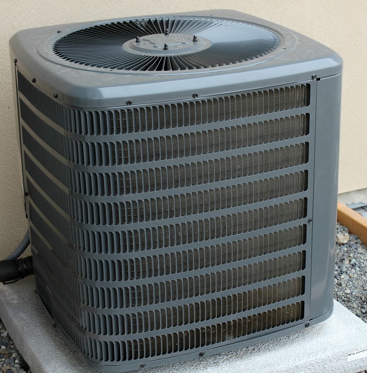 Outdoor air conditioning unit with gray metal grilles and a top fan on a concrete pad