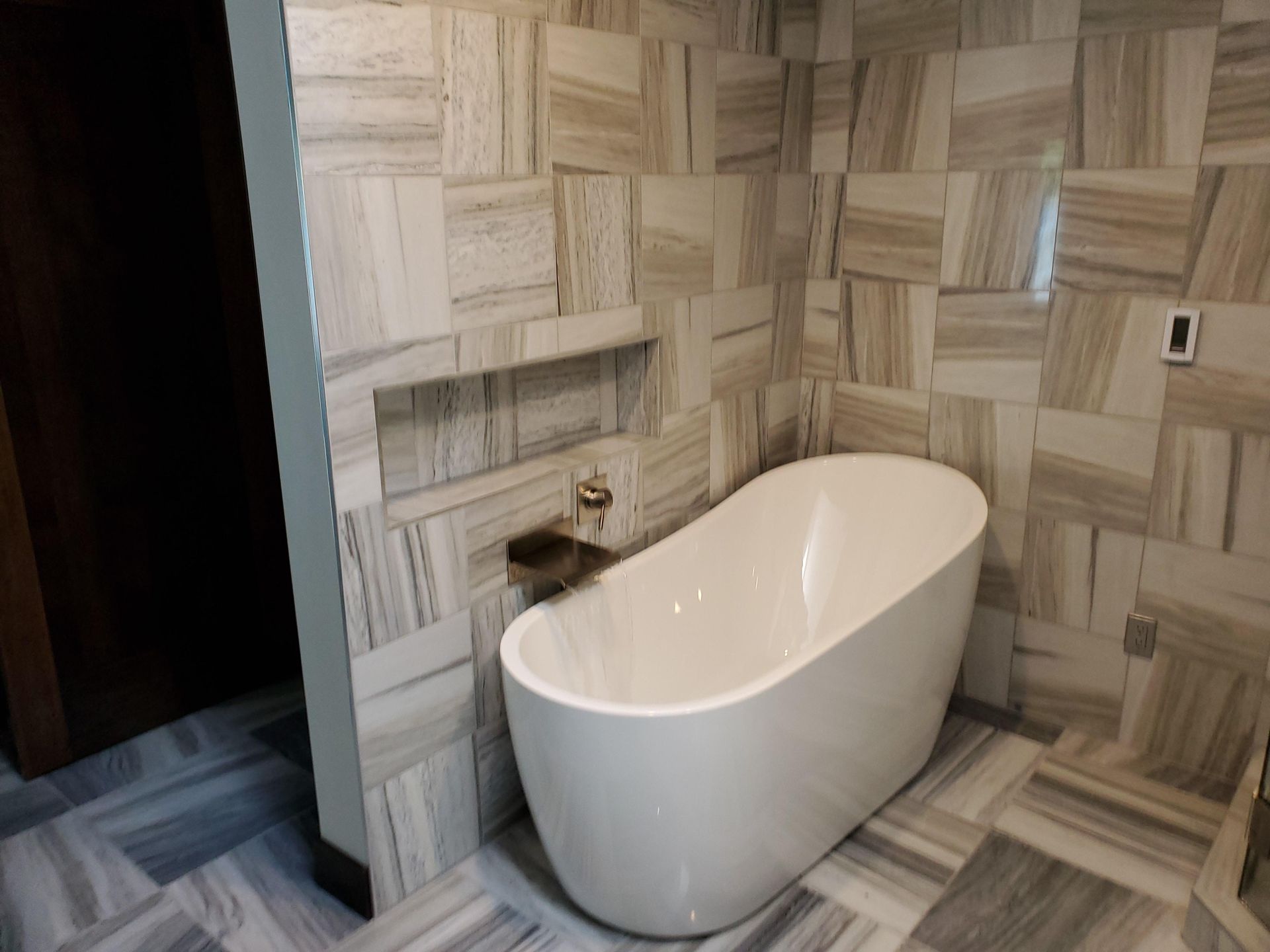 Modern bathroom with a white freestanding tub and wood-pattern tile walls and floor.