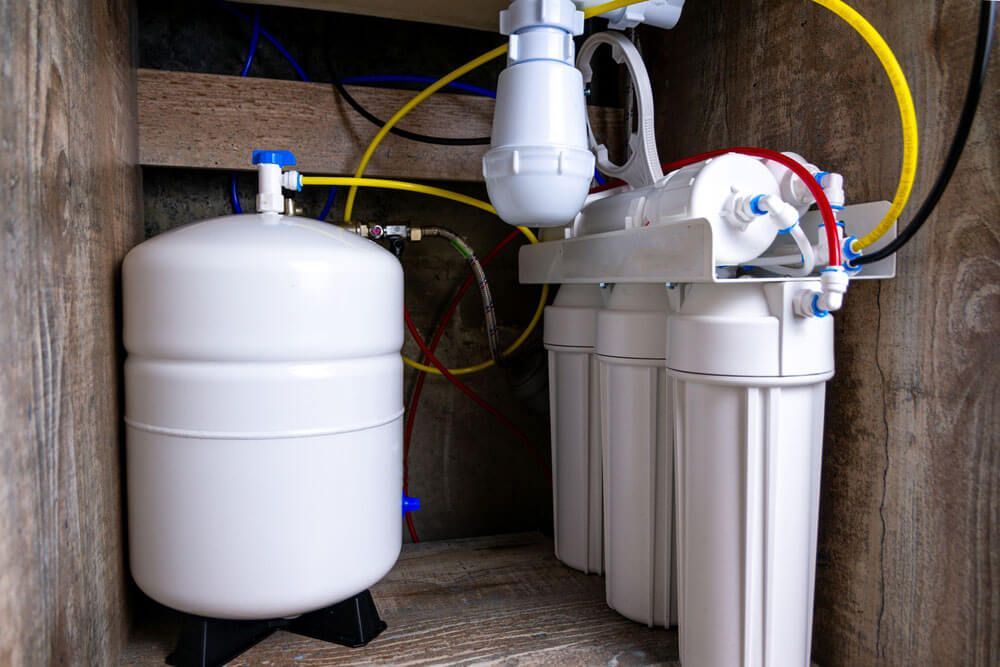 Water filtration system with white tanks, pipes, and yellow tubing installed in a wooden utility space