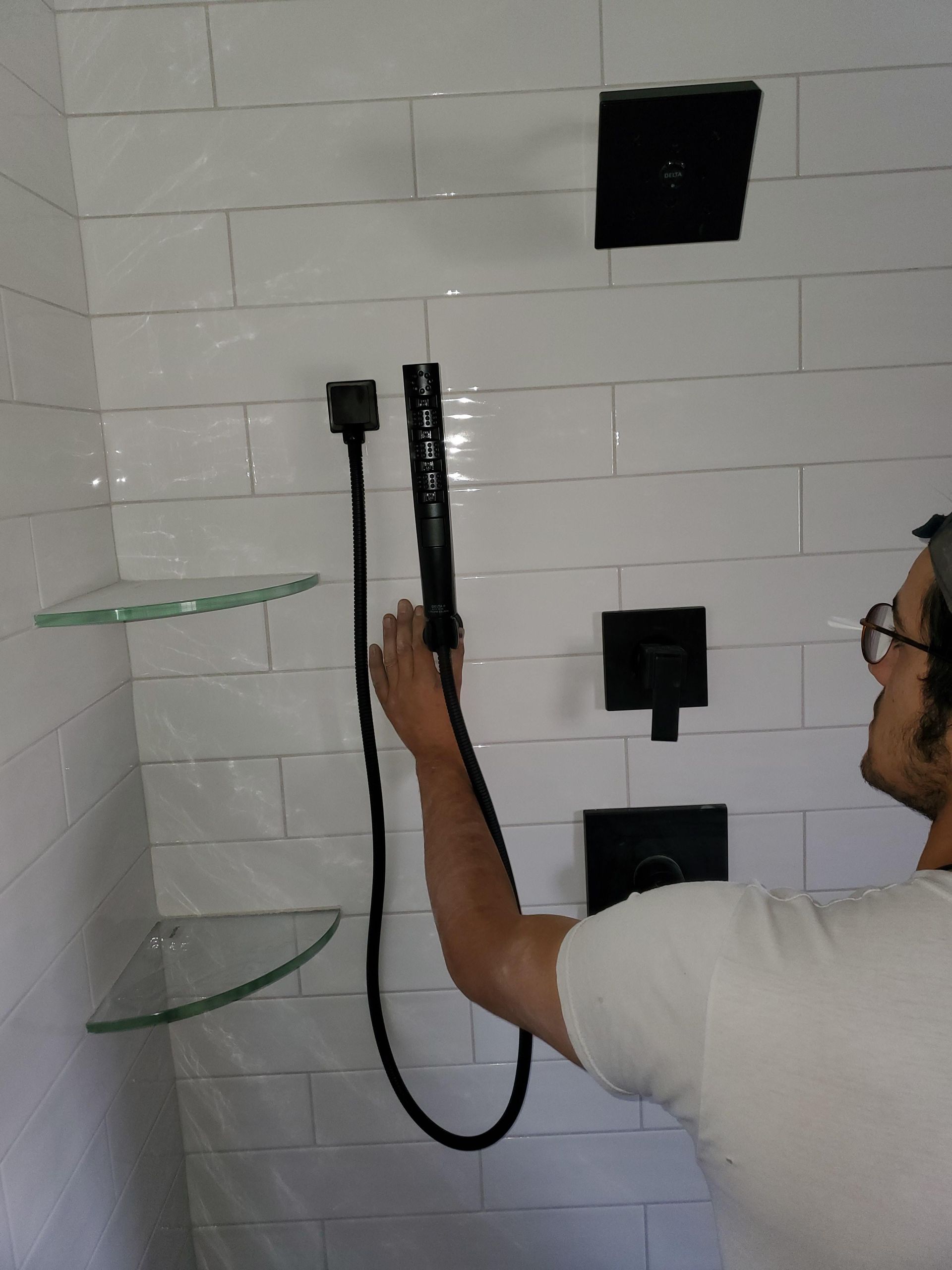 Person pointing at a shower fixture and hose on a tiled wall in a bathroom