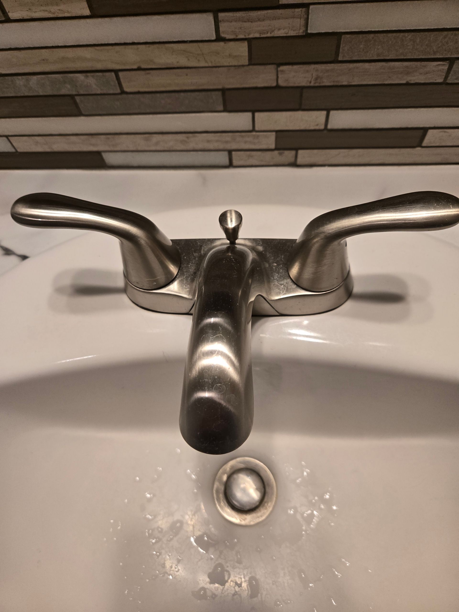 Chrome bathroom sink faucet with two handles and a drain below on a white sink.