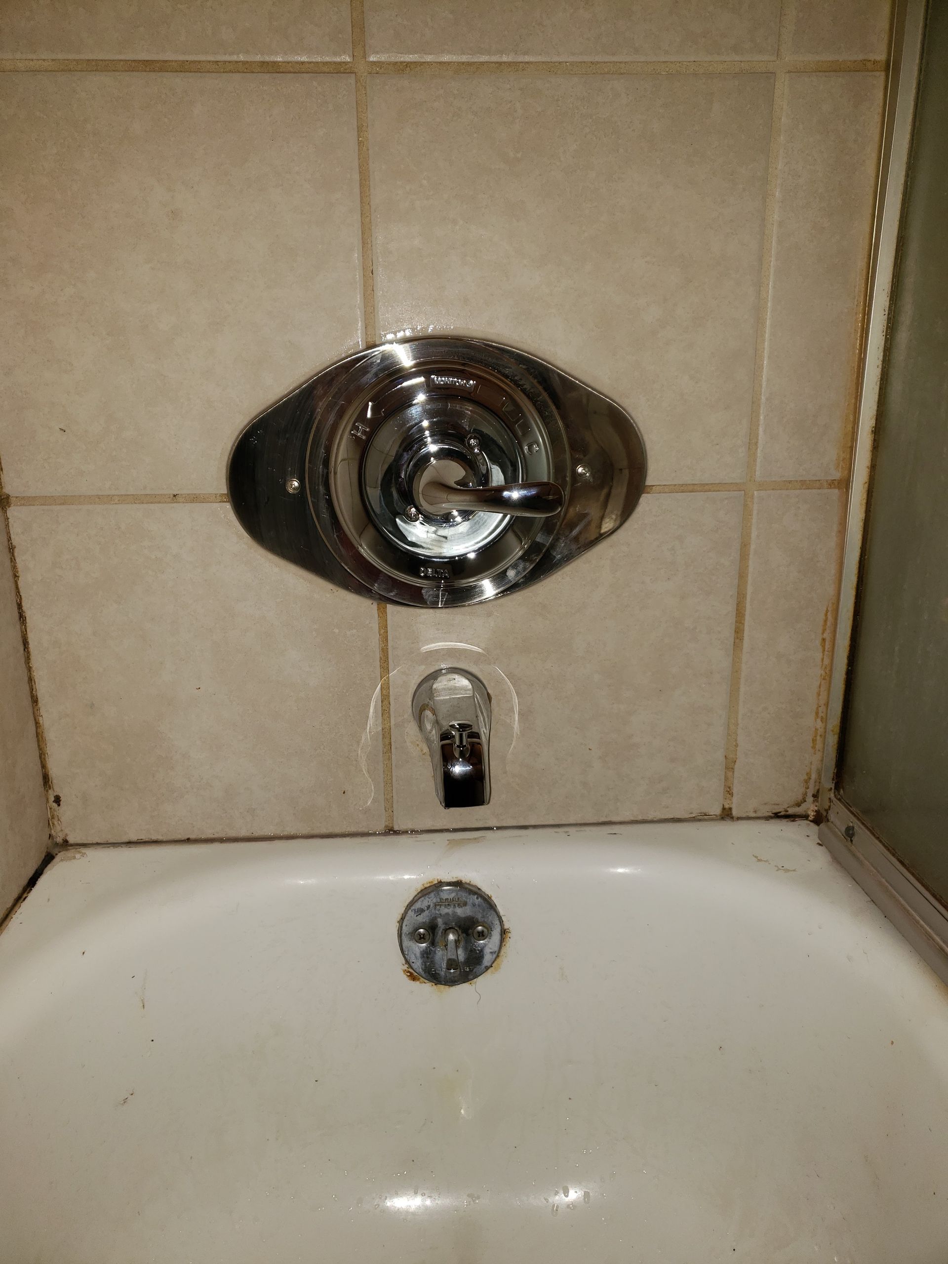 Bathroom tub with chrome shower controls and beige tiled wall above the faucet.