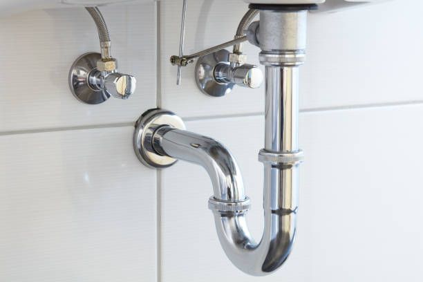 Chrome sink drain pipes under a white bathroom sink on tiled wall