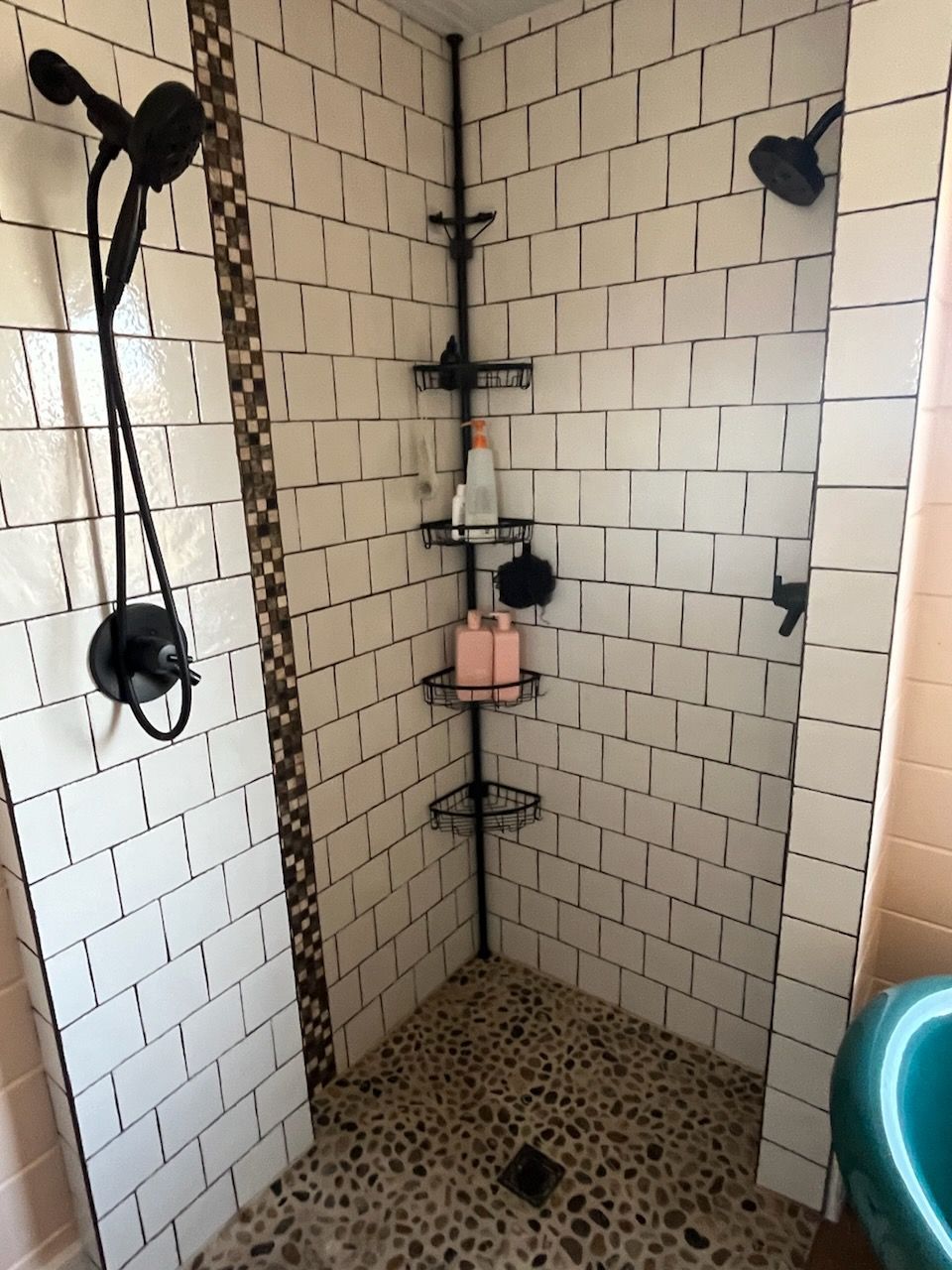 Small tiled shower stall with a corner shelf, showerhead, and floor drain.