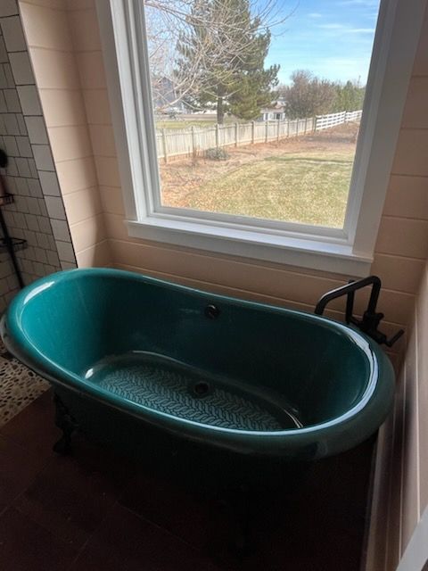 Teal oval bathtub beneath a window in a bathroom, with a black faucet on the right.