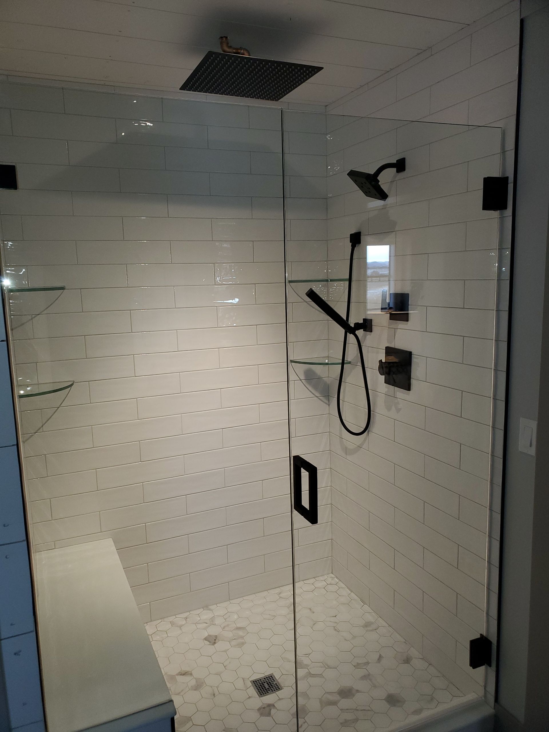 White tiled shower stall with glass door, black shower fixtures, and a ceiling vent.