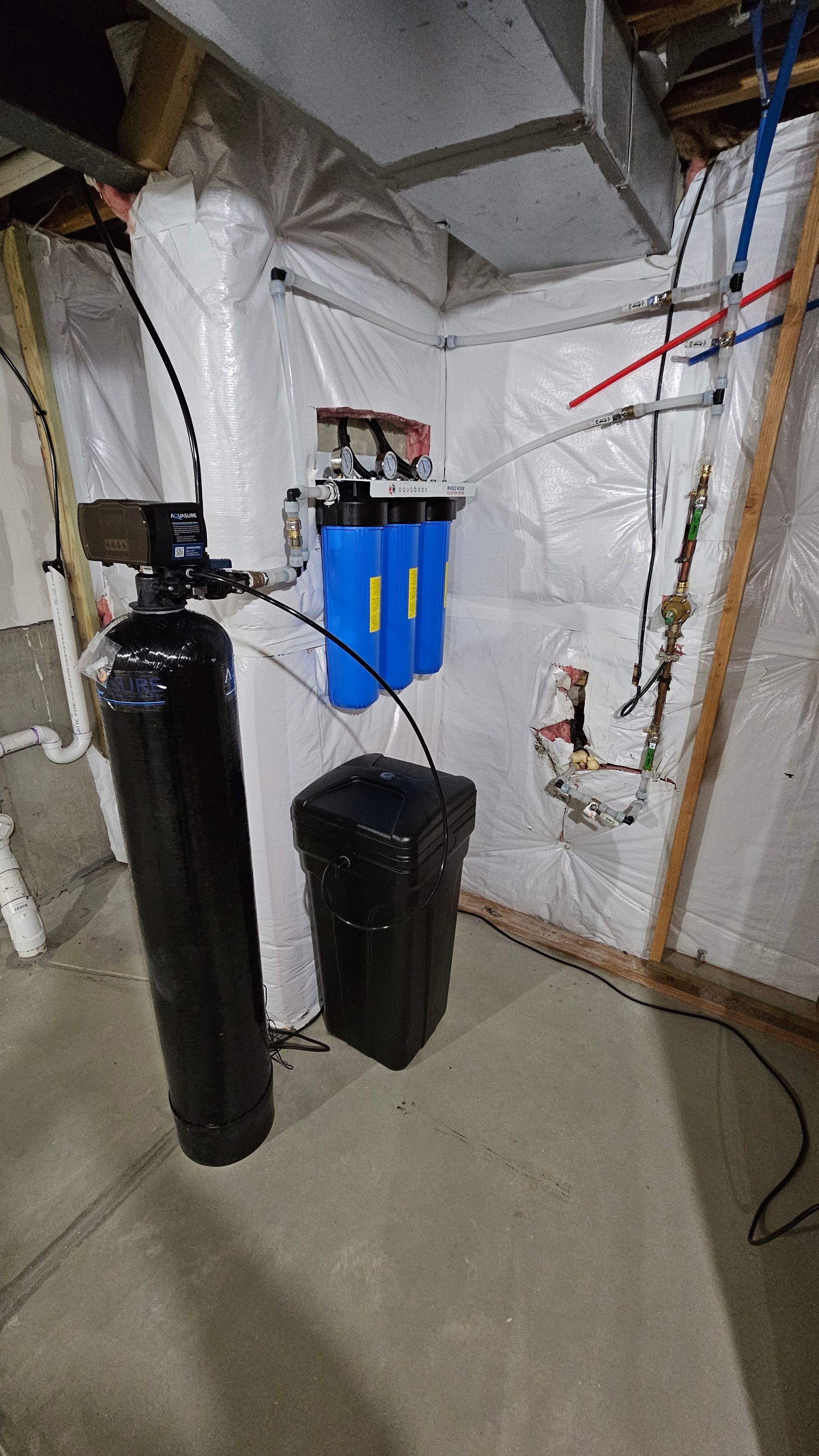 Utility room with water filtration tanks, blue filter units, and exposed pipes against a wall.