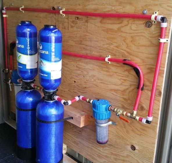 Blue water filter system with four canisters and red pipes mounted on a wooden wall