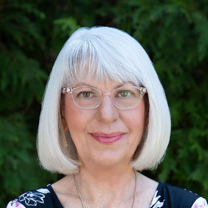 a woman with white hair and glasses is smiling for the camera .
