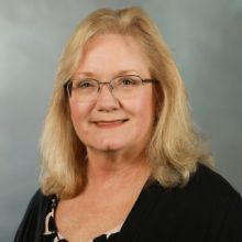 a woman with long blonde hair is wearing a black shirt and a necklace .