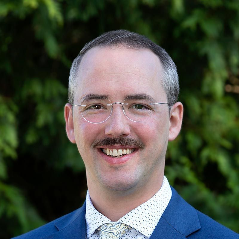 a man with a mustache and glasses is wearing a blue suit and tie .