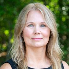 a woman with long blonde hair is wearing a black shirt and a necklace .