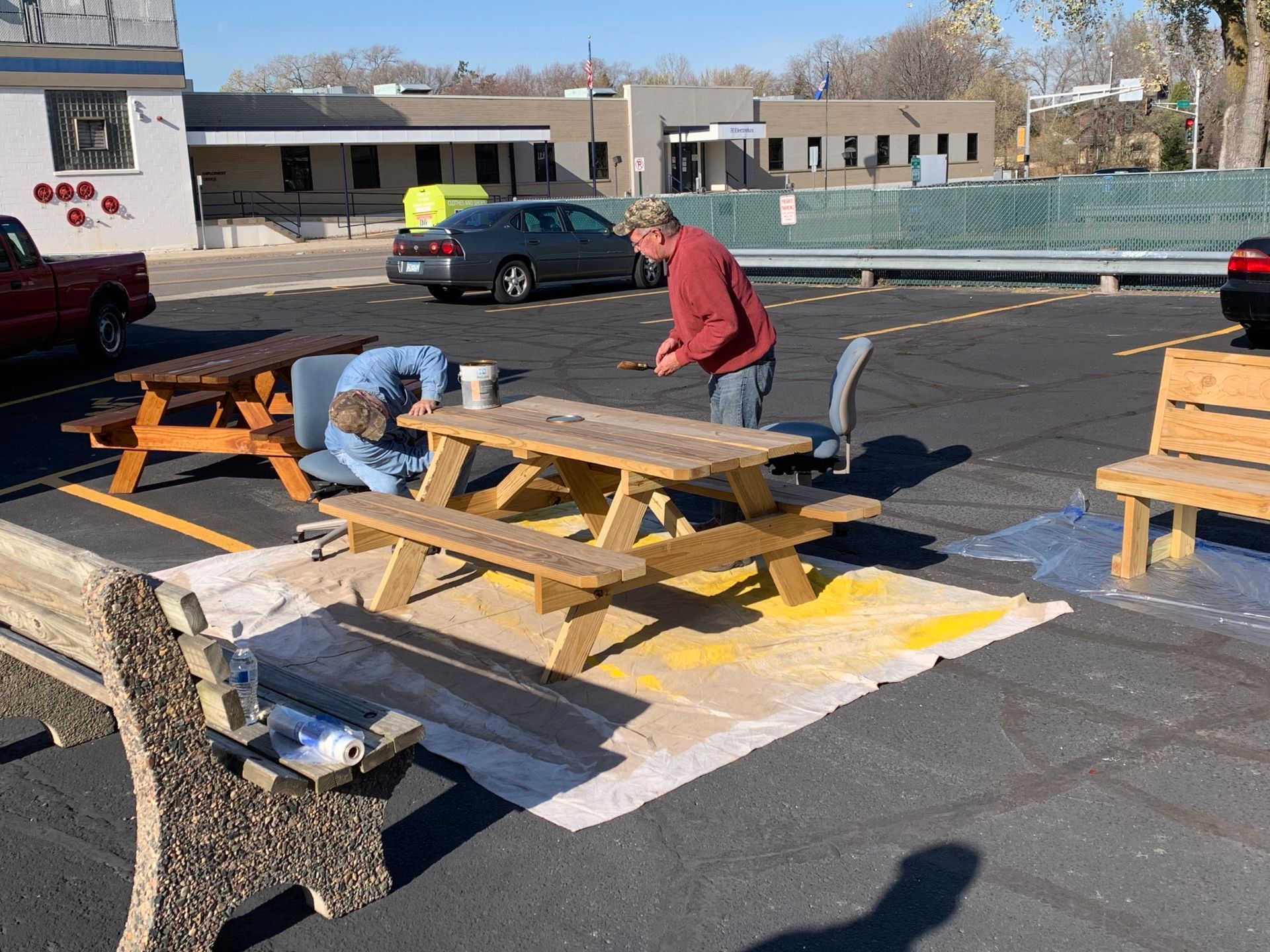 A man is painting a picnic table in a parking lot
