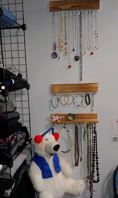 A stuffed polar bear wearing a blue scarf is sitting next to a jewelry rack.