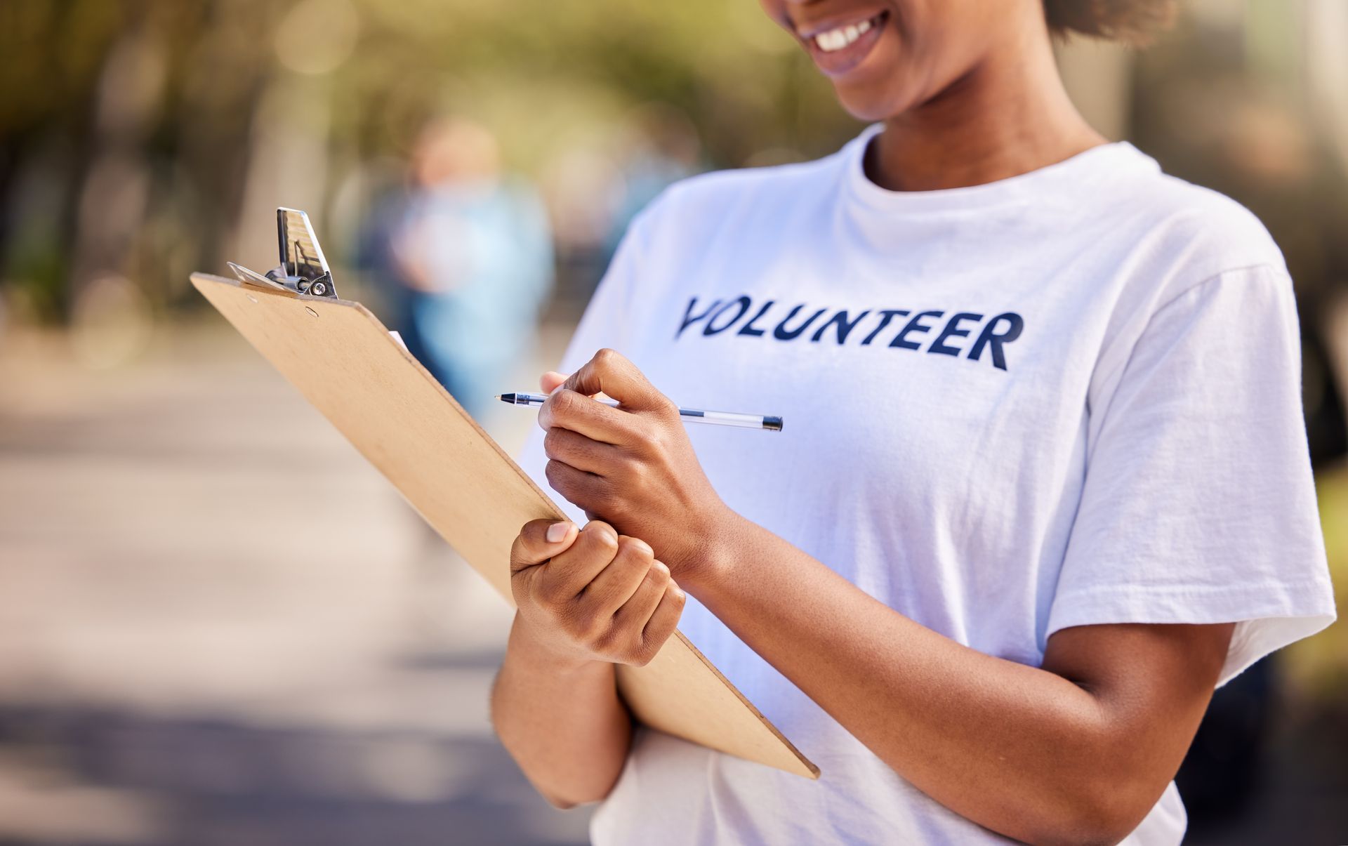 A woman in a volunteer shirt is holding a clipboard and writing on it.