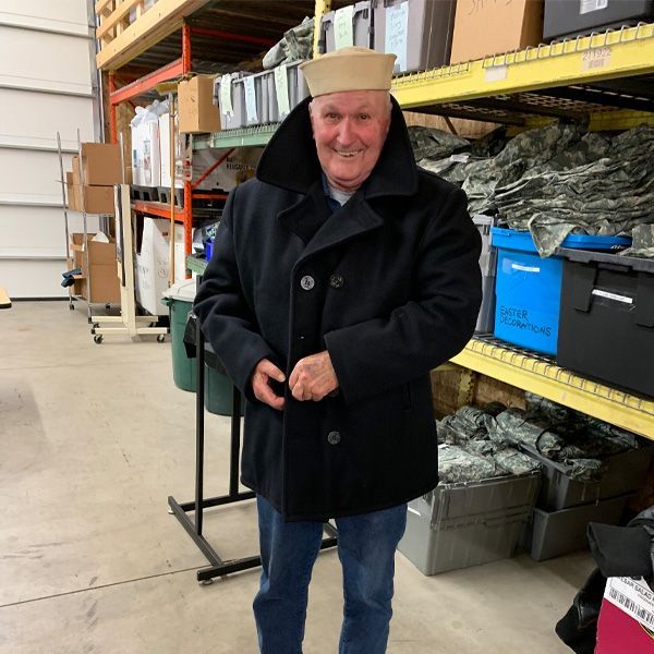 A man wearing a hat and a black coat is standing in a warehouse