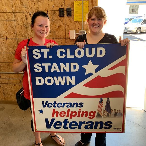 Two women holding a sign that says st cloud stand down veterans helping veterans