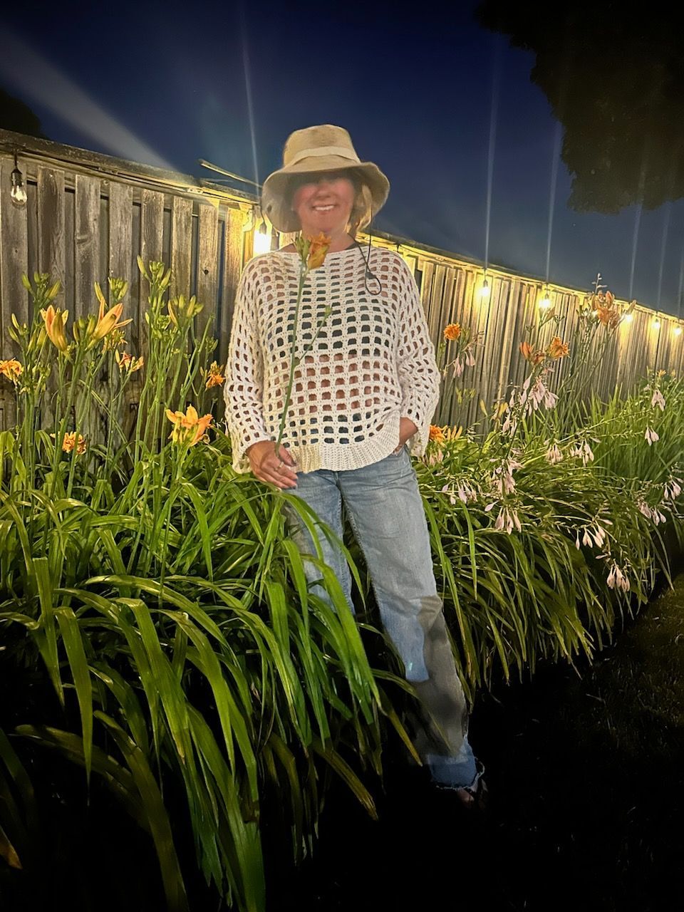 A woman in a cowboy hat is standing in a garden with flowers.