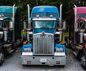 three semi trucks are parked next to each other on gravel .