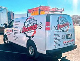 Foccus Road Service white van with a wrench on the roof is parked in a parking lot .