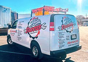 a white van with a wrench on the roof is parked in a parking lot .