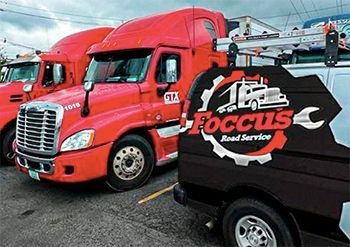 a row of red trucks parked next to a black van that says focus road service