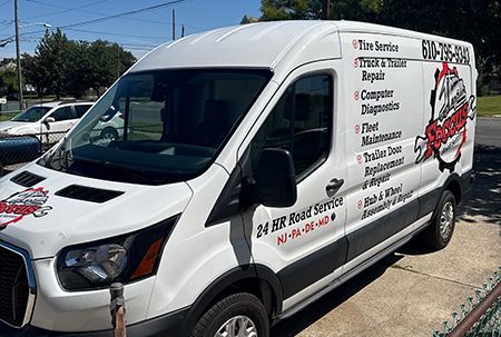 White service van with tire service logo, parked outdoors. Black trim. Services include truck repair and trailer work.