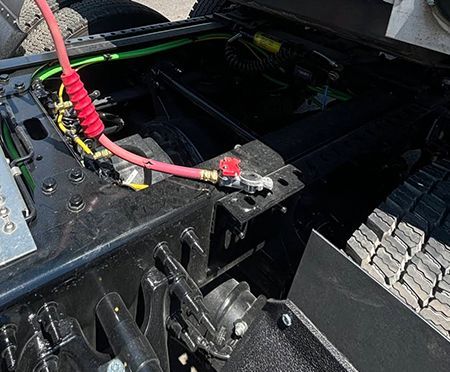 Underside of a black truck chassis with a red air hose connected to a battery terminal.