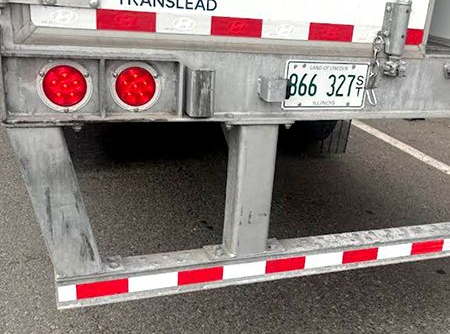 Rear view of a semi-trailer with red and white reflective tape, red lights, and a license plate: 866 327.