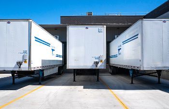 a row of white semi trucks are parked in a parking lot .