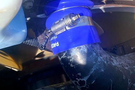 Blue silicone hose connected to black pipe with a metal clamp in an engine bay.