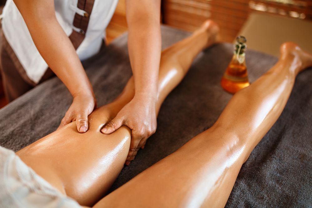 Massage Therapist Massaging Legs with Oil on A Spa Table — Pink Lily Beauty in Blacksmiths, NSW