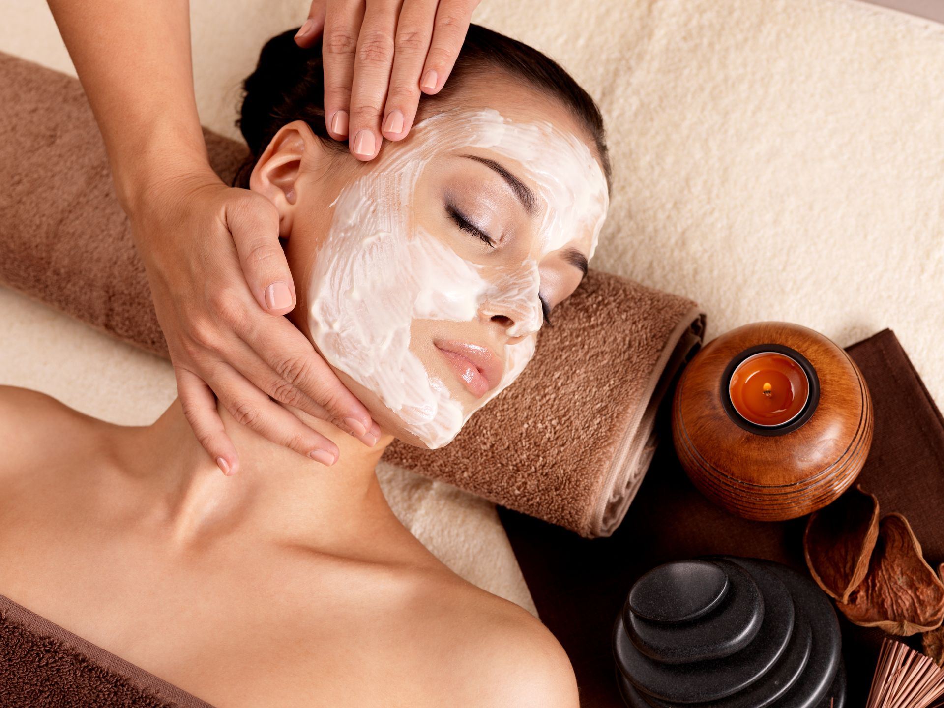 A Person With a White Facial Mask Lies on a Towel While Receiving a Facial Massage — Pink Lily Beauty in Blacksmiths, NSW