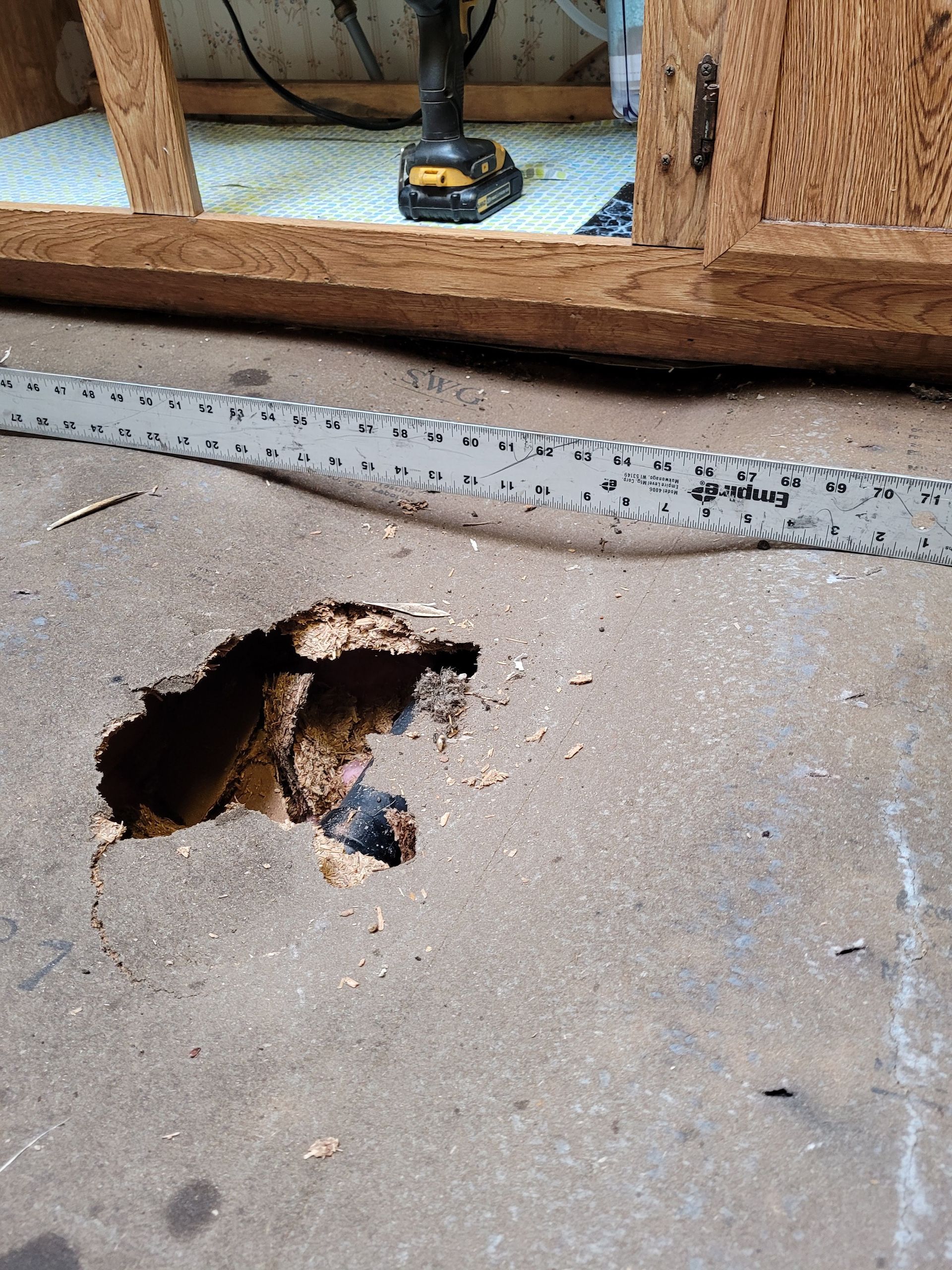 A hole in the floor next to a ruler and a drill.