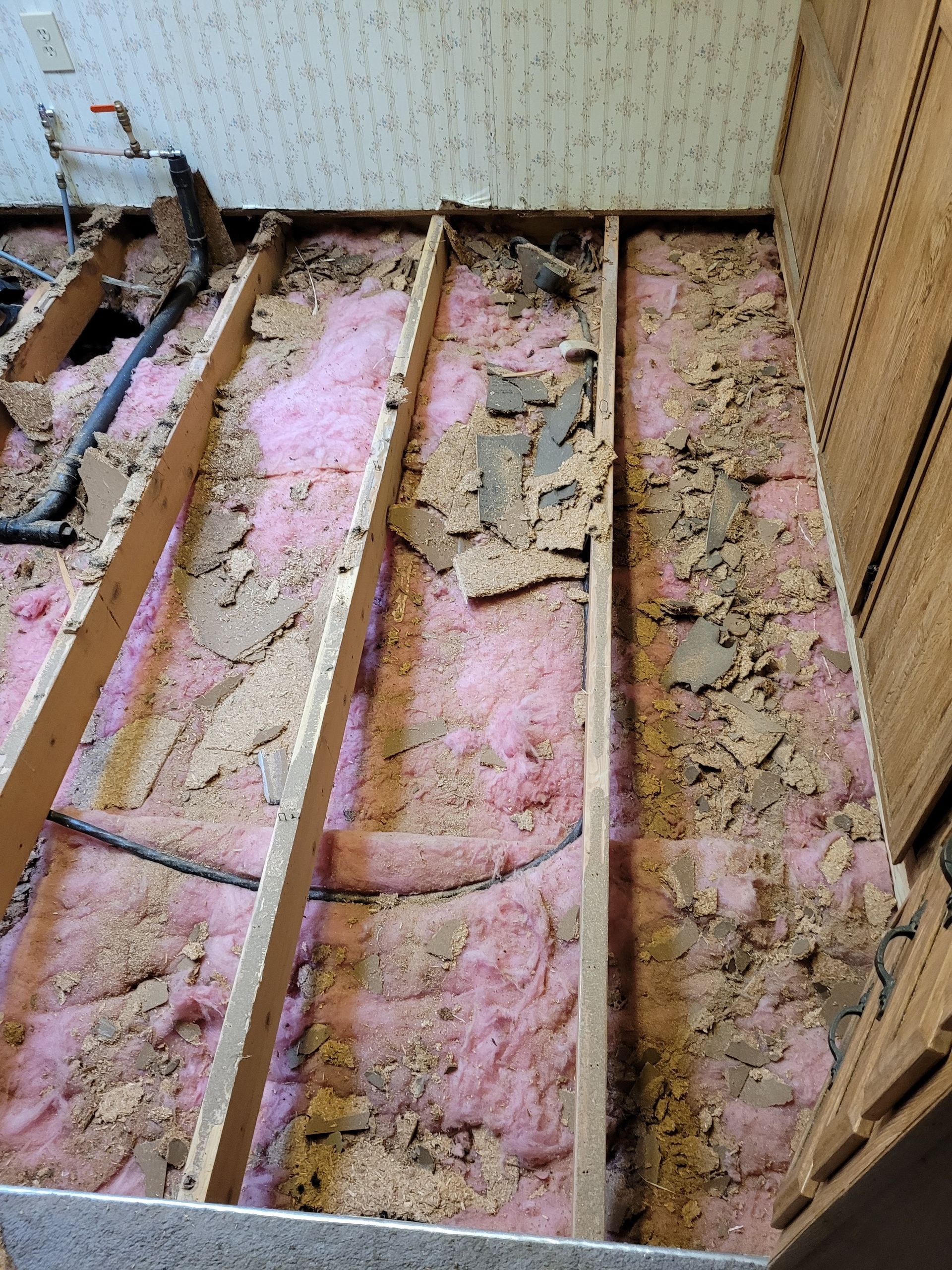 A room with a lot of wood and pink insulation on the floor.