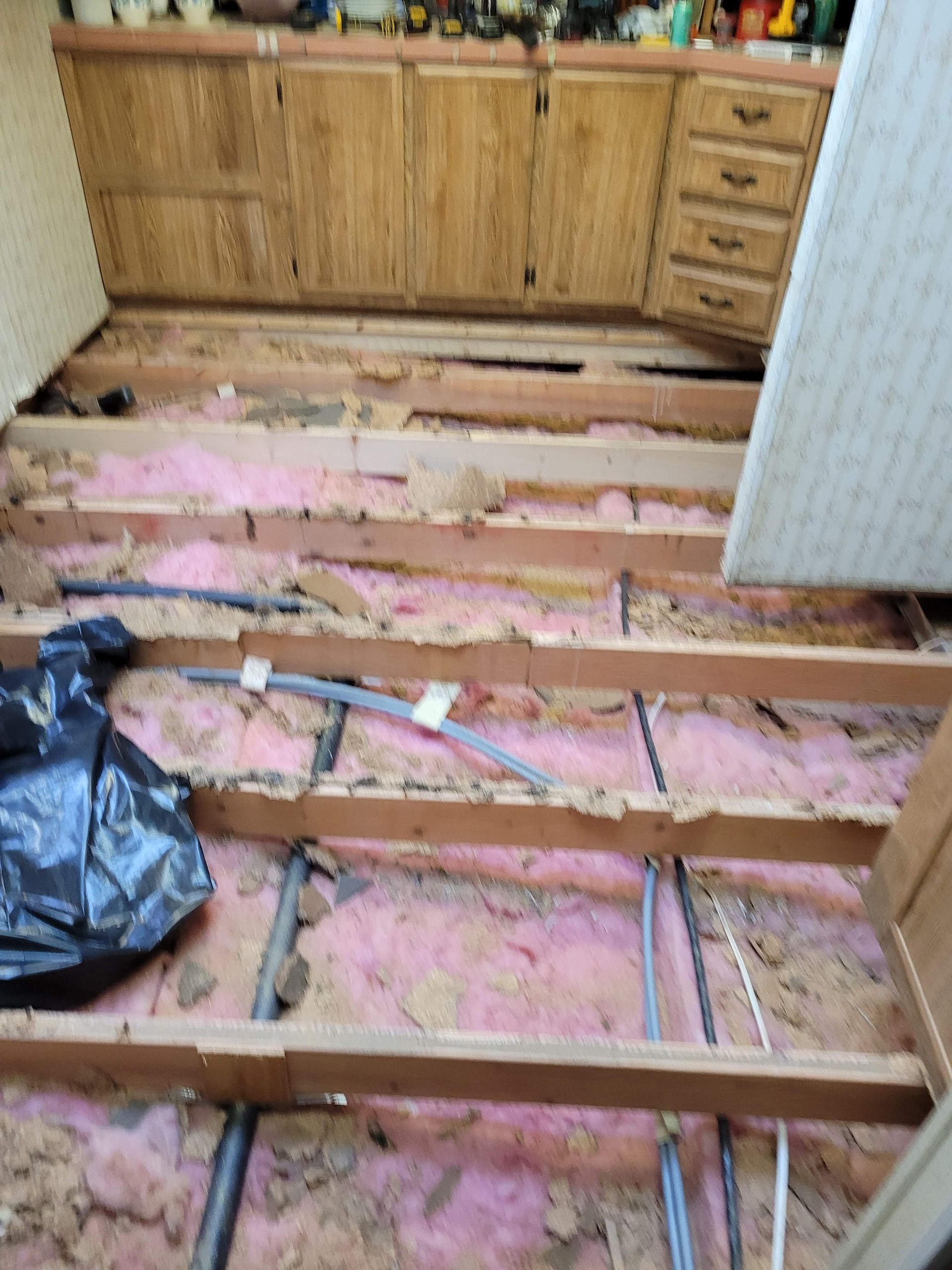 A kitchen floor with wooden beams and pink insulation.